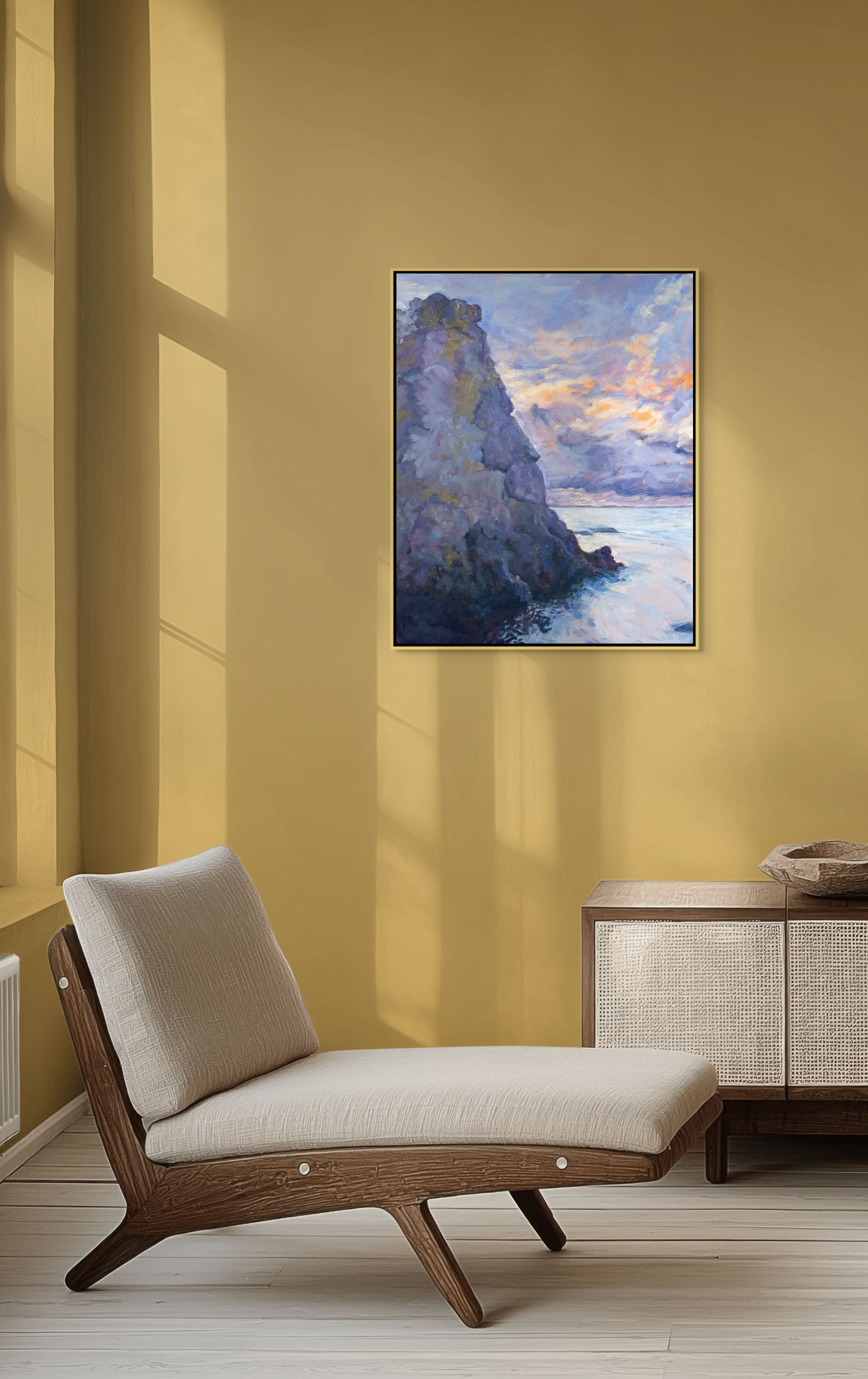 Stone Giant oil painting by Sally Herriott, solitary rauk sea stack rising from calm Baltic water at sunset, displayed in a warm yellow lounge with easy modern chair and sideboard.